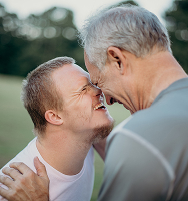 A father and son touch foreheads and smile at each other, with a green field in the background